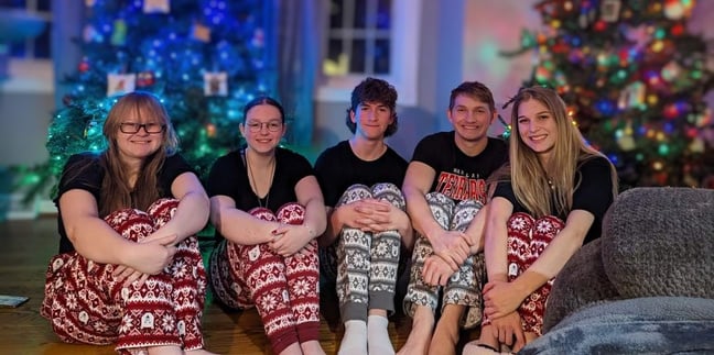 a group five people wearing pajamas sitting on the floor in front of a Christmas tree