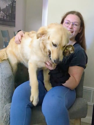 a person sitting on a couch holding a Golden Retriever puppy.