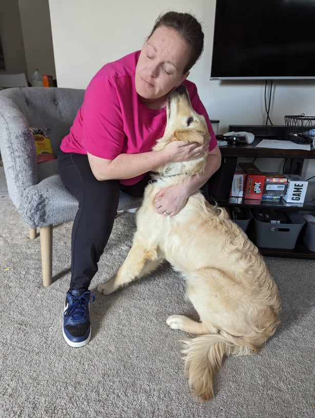 a person in a pink shirt petting a golden retriever